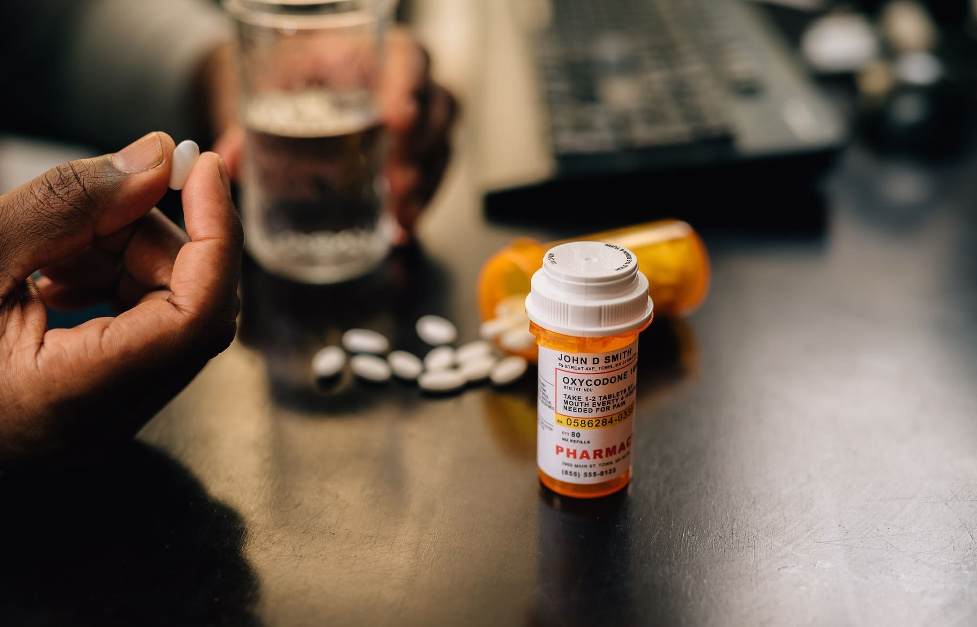 Bottles of narcotic pills spilled on table, man in background with glass of water