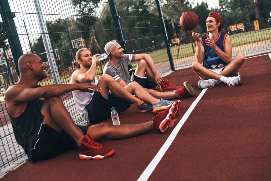 diverse group of men sitting on basketball court. people in intensive outpatient programs can continue doing their hobbies.